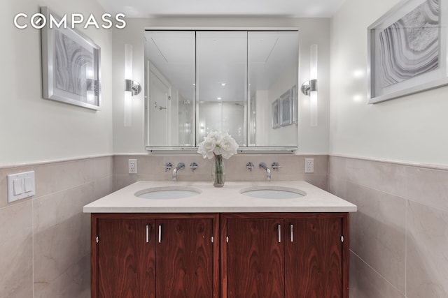 full bath with wainscoting, a sink, double vanity, and tile walls