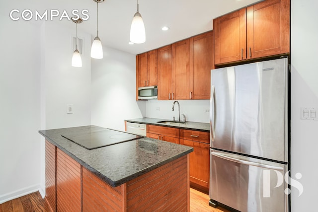 kitchen featuring stainless steel appliances, a sink, light wood-style floors, brown cabinets, and recessed lighting