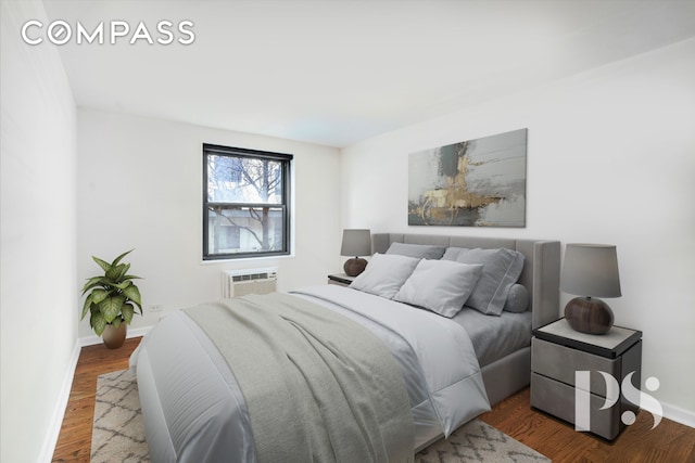 bedroom with a wall unit AC, baseboards, and wood finished floors