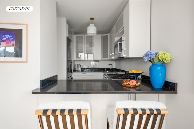 181 7th Ave Unit 14A, New York City, NY 10011 - kitchen featuring stainless steel microwave, dark countertops, glass insert cabinets, and a peninsula