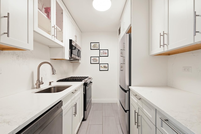 kitchen with stainless steel appliances, white cabinets, a sink, glass insert cabinets, and light stone countertops
