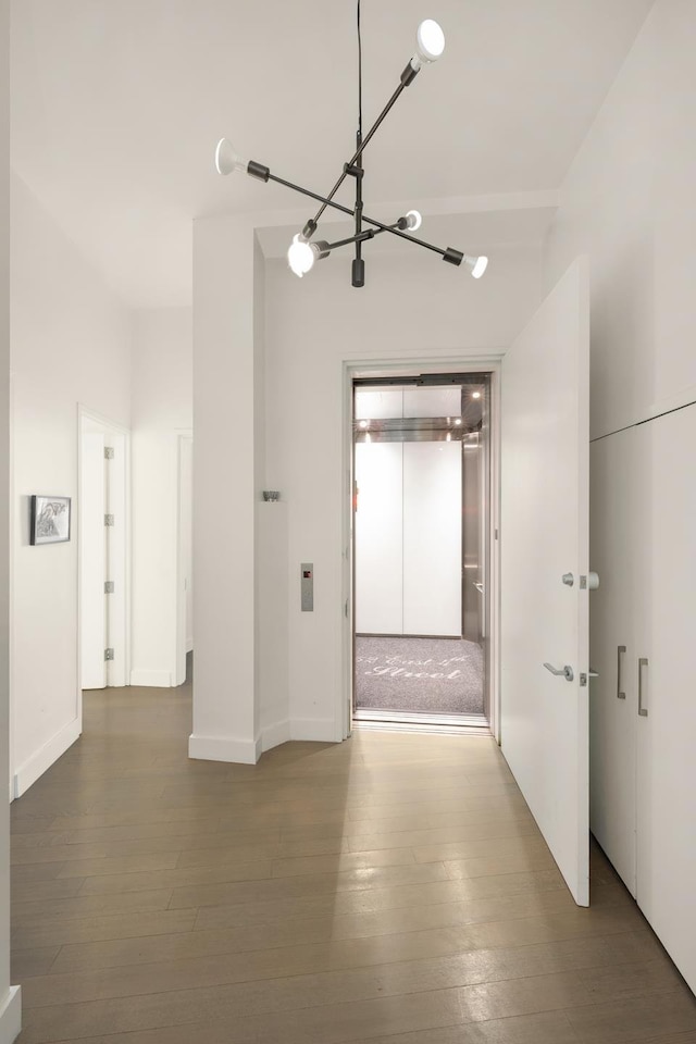 corridor with hardwood / wood-style floors, elevator, and a chandelier