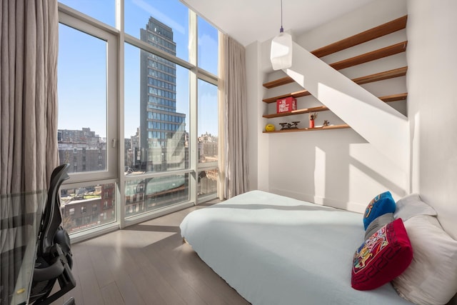 bedroom with multiple windows, a city view, a wall of windows, and wood finished floors
