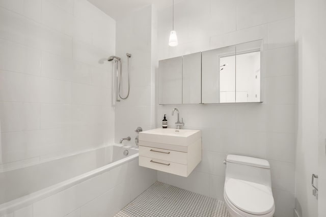 bathroom with tile walls, toilet, vanity, tiled shower / bath, and tile patterned flooring