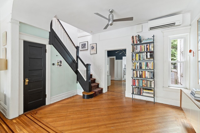 foyer featuring ceiling fan, a wall unit AC, stairway, and light wood-type flooring