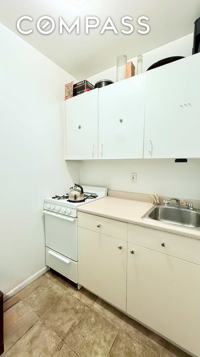 229 E 29th St Unit 5H, New York City, NY 10016 - kitchen with white gas stove, a sink, white cabinets, light countertops, and baseboards