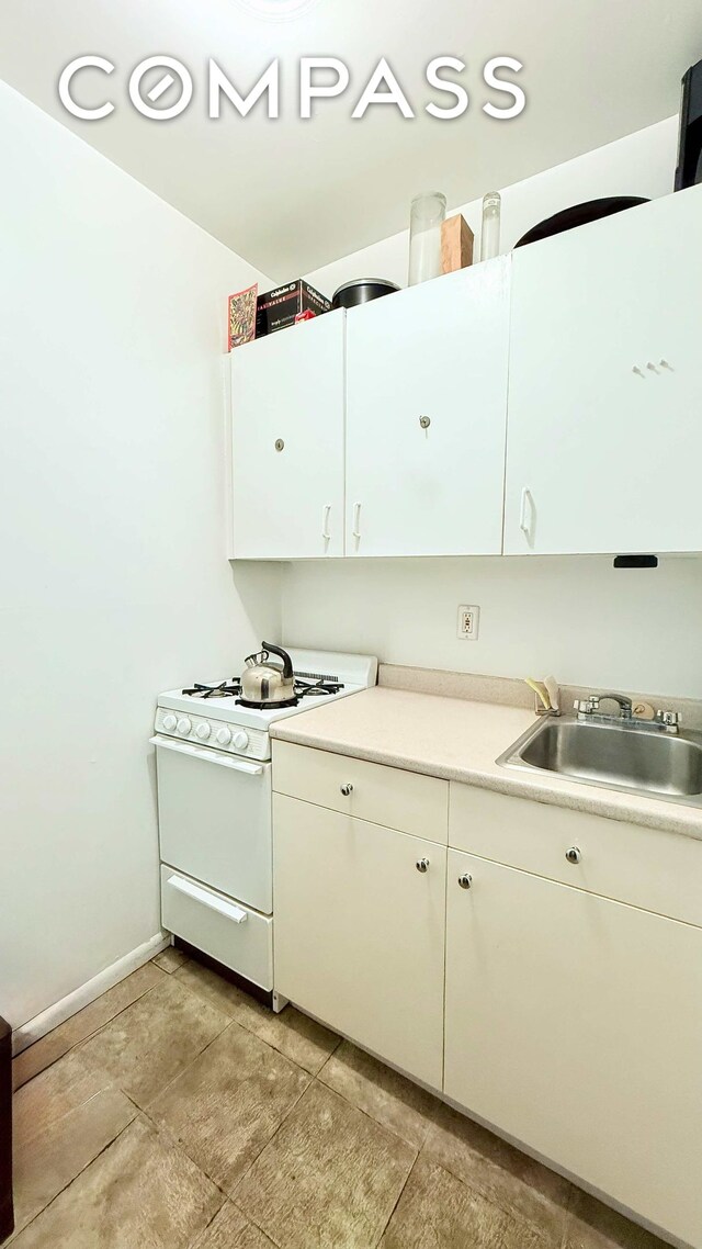 kitchen with white cabinetry, gas range gas stove, light countertops, a sink, and baseboards