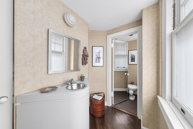 bathroom with wallpapered walls, toilet, a sink, baseboards, and hardwood / wood-style flooring