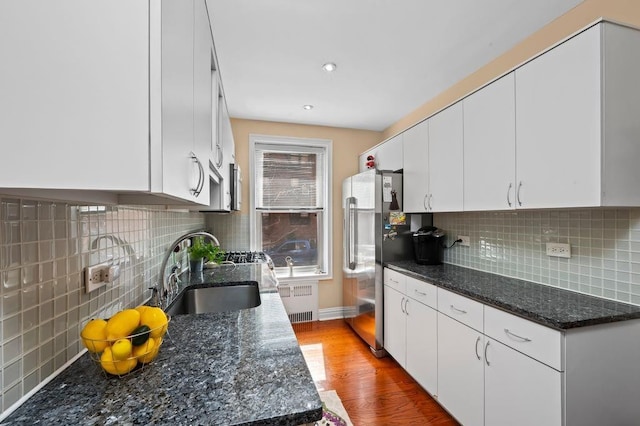 kitchen with freestanding refrigerator, a sink, wood finished floors, radiator heating unit, and tasteful backsplash