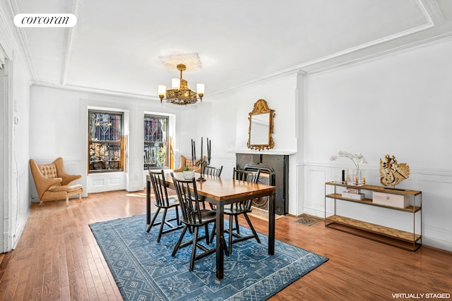 dining space featuring a fireplace, a chandelier, wood finished floors, ornamental molding, and a decorative wall