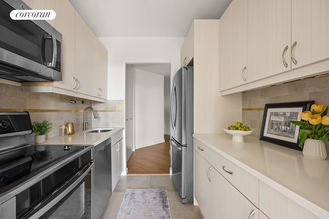 kitchen featuring appliances with stainless steel finishes, a sink, light countertops, tasteful backsplash, and light tile patterned floors