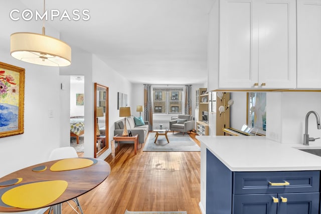 100 Overlook Ter Unit 85, New York City, NY 10040 - kitchen with blue cabinetry, light wood-type flooring, light countertops, pendant lighting, and white cabinets