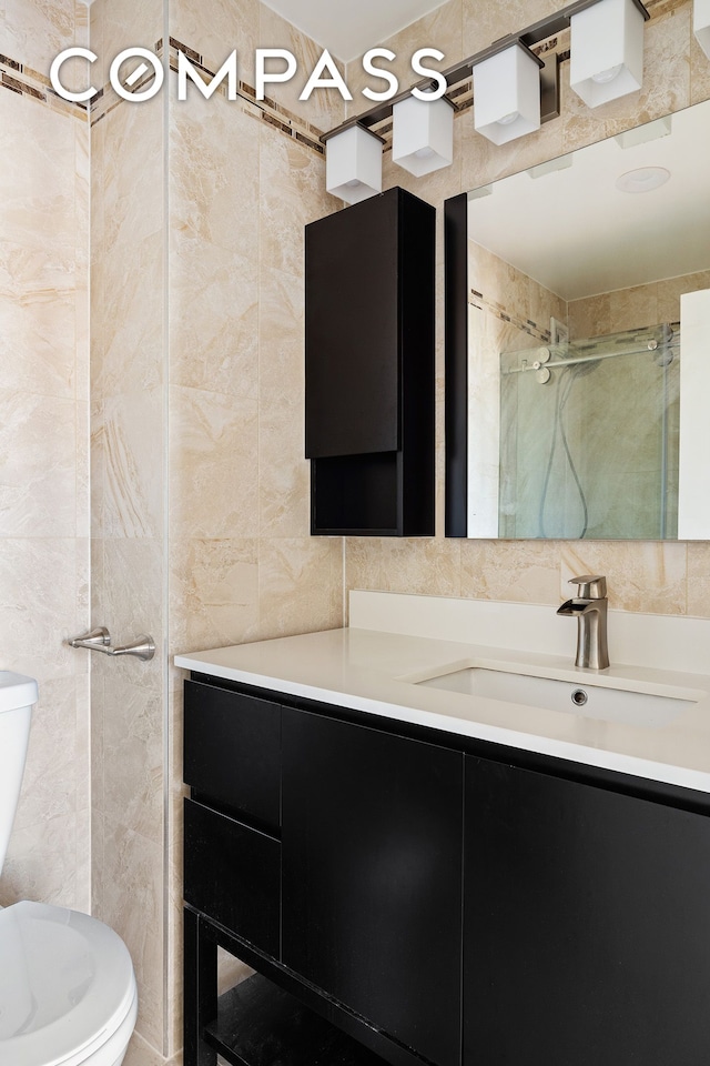 bathroom with toilet, a stall shower, tile walls, and vanity