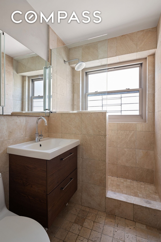 full bathroom featuring tile walls, a tile shower, healthy amount of natural light, vanity, and toilet
