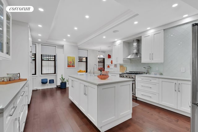 kitchen featuring appliances with stainless steel finishes, wall chimney range hood, a raised ceiling, crown molding, and white cabinets