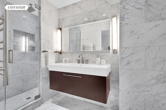 bathroom featuring a marble finish shower, vanity, tile walls, and a towel warmer
