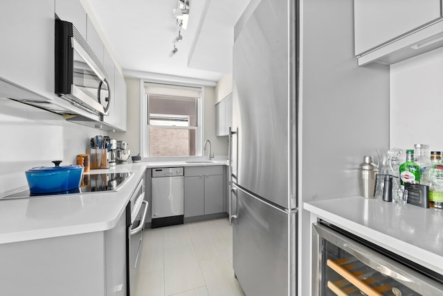 kitchen featuring appliances with stainless steel finishes, a sink, gray cabinetry, wine cooler, and light countertops