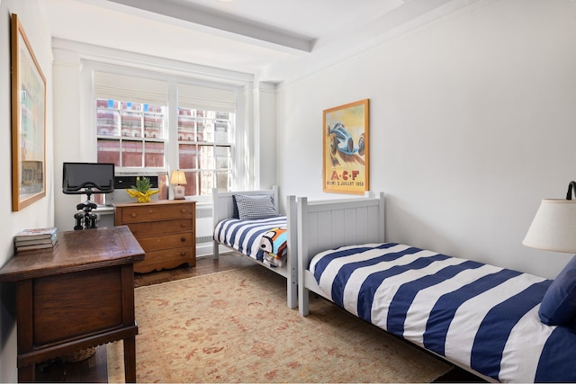 bedroom with beamed ceiling and wood finished floors