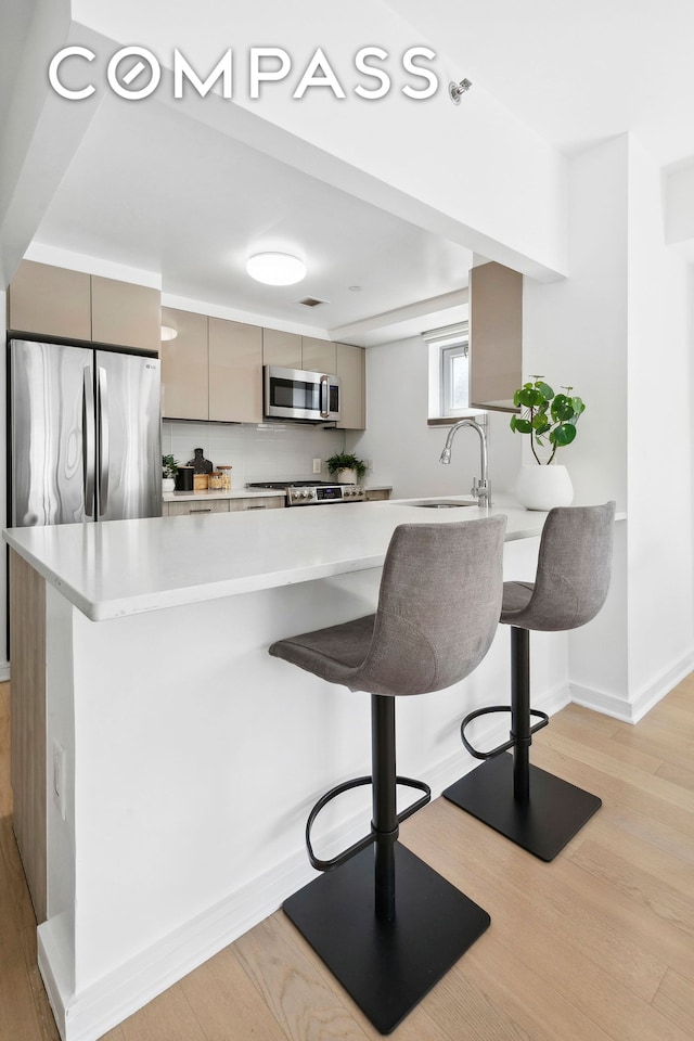 kitchen with appliances with stainless steel finishes, a sink, a breakfast bar area, and light wood finished floors