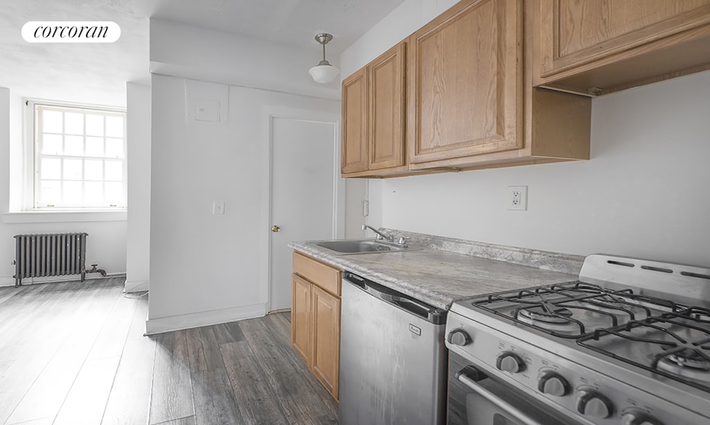 kitchen with a sink, radiator heating unit, dishwashing machine, gas range, and visible vents