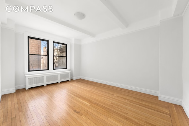 empty room featuring light wood-style floors, baseboards, radiator heating unit, and beam ceiling