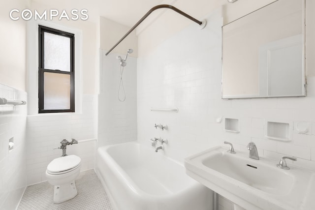 bathroom with tile walls, a sink, a wainscoted wall, toilet, and washtub / shower combination