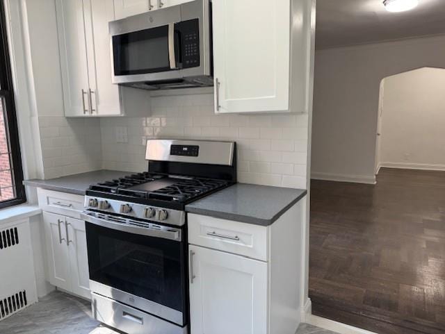 2515 Glenwood Rd Unit 2E, New York City, NY 11210 - kitchen featuring appliances with stainless steel finishes, white cabinetry, radiator, decorative backsplash, and dark countertops