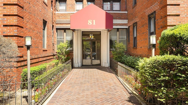 view of exterior entry featuring brick siding and fence