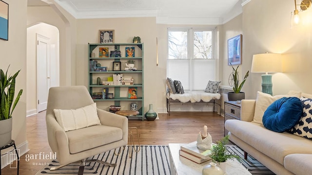 living area with crown molding, arched walkways, baseboards, and wood finished floors