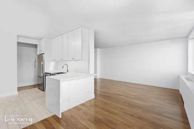30 W 61st St Unit 24C, New York City, NY 10023 - kitchen with light wood-type flooring, light countertops, a sink, white cabinets, and stainless steel fridge