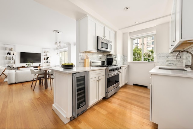kitchen featuring appliances with stainless steel finishes, beverage cooler, a sink, white cabinetry, and light countertops