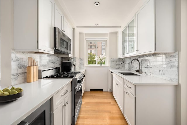 kitchen with stainless steel appliances, a sink, light countertops, white cabinets, and light wood finished floors