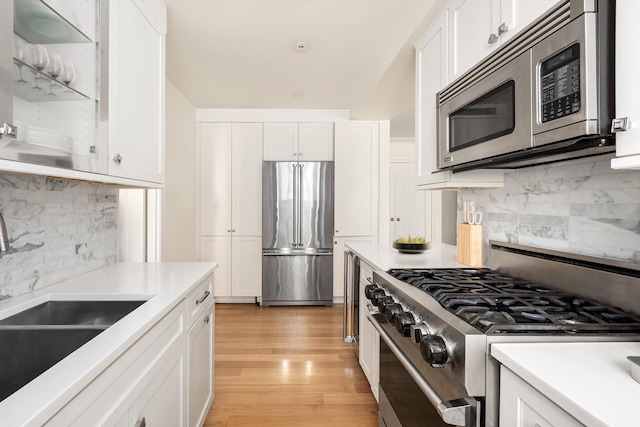 kitchen with stainless steel appliances, a sink, tasteful backsplash, white cabinetry, and light wood-style flooring
