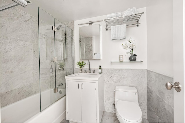 full bath with toilet, tile walls, combined bath / shower with glass door, a wainscoted wall, and vanity