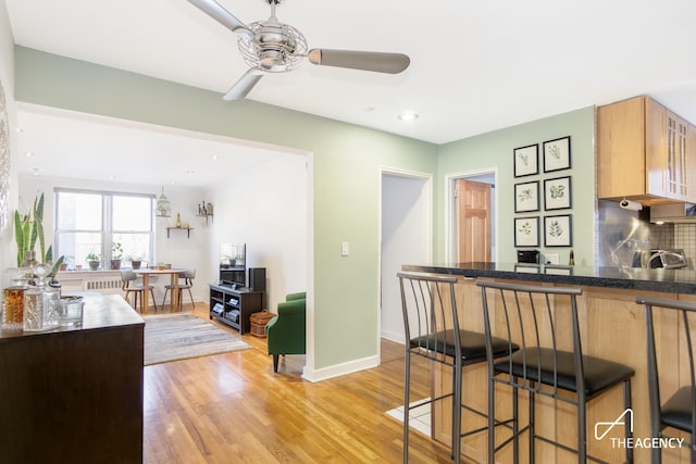 153 Bennett Ave Unit 3G, New York City, NY 10040 - kitchen featuring a ceiling fan, a kitchen bar, light wood finished floors, baseboards, and backsplash