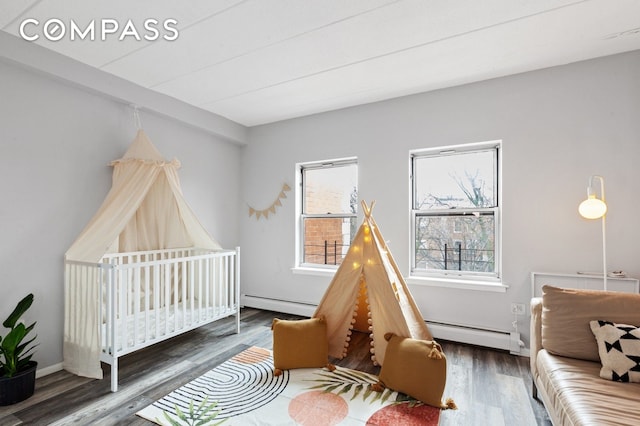 bedroom with baseboard heating, wood finished floors, and a crib