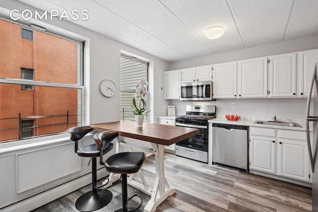 kitchen featuring stainless steel appliances, a sink, light wood-style flooring, white cabinets, and light countertops