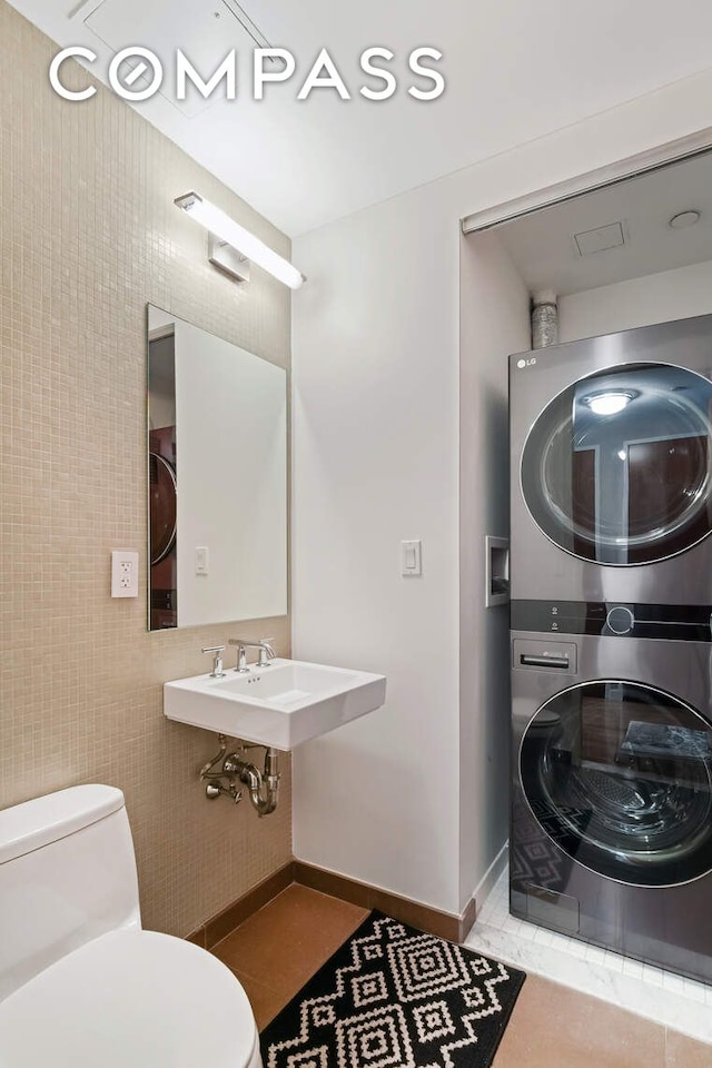 454 W 54th St Unit 3D, New York City, NY 10019 - bathroom featuring estacked washer and dryer, toilet, a sink, and tile patterned flooring