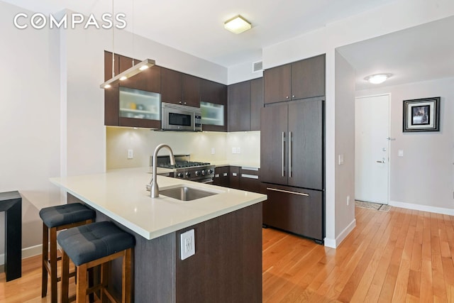 454 W 54th St Unit 3D, New York City, NY 10019 - kitchen featuring high end appliances, a peninsula, a breakfast bar, dark brown cabinetry, and light countertops