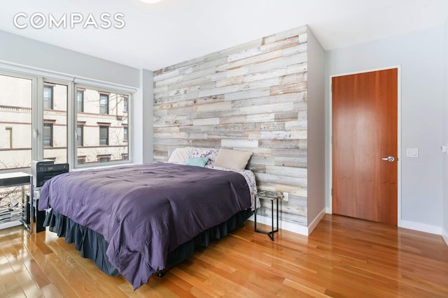 454 W 54th St Unit 3D, New York City, NY 10019 - bedroom featuring an accent wall, wood finished floors, wood walls, and baseboards