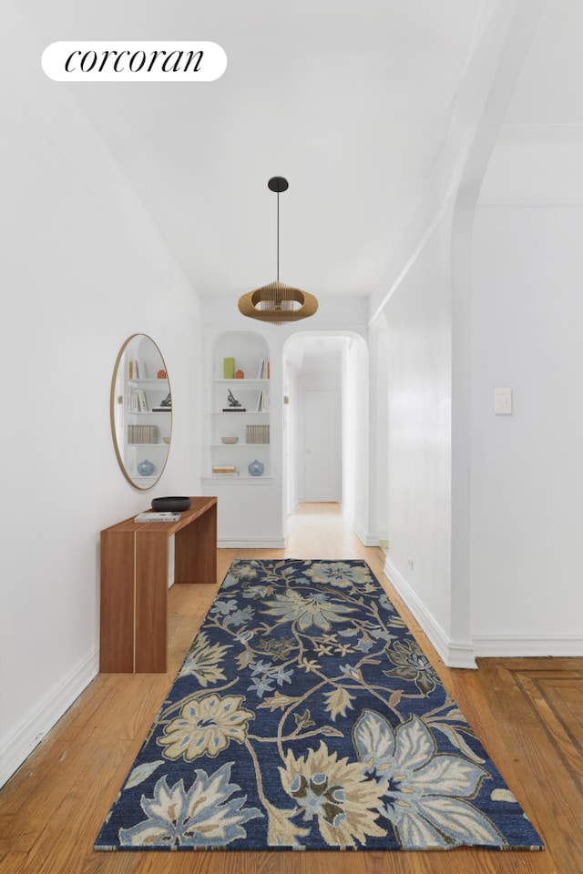 hall with built in features, arched walkways, baseboards, and wood finished floors