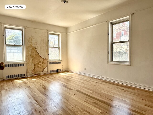 empty room with radiator, wood finished floors, and plenty of natural light