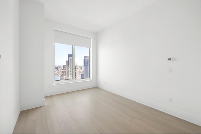 unfurnished room featuring baseboards, light wood-style flooring, and a view of city