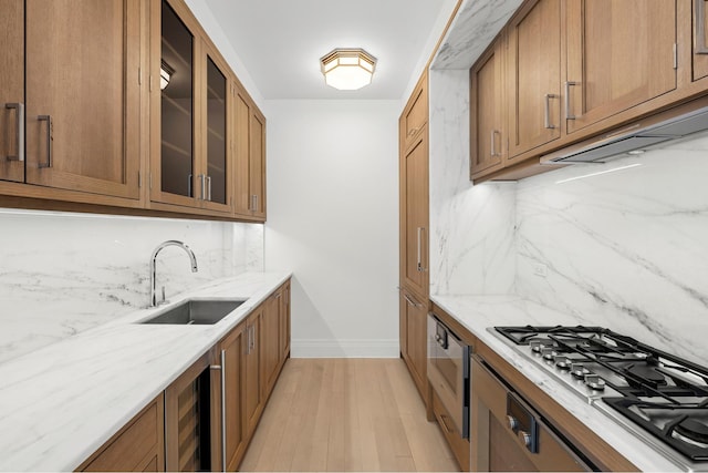 kitchen featuring brown cabinetry, backsplash, stainless steel gas cooktop, a sink, and beverage cooler