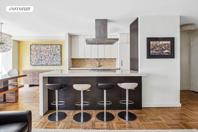 kitchen featuring tasteful backsplash, island range hood, a kitchen bar, and light countertops