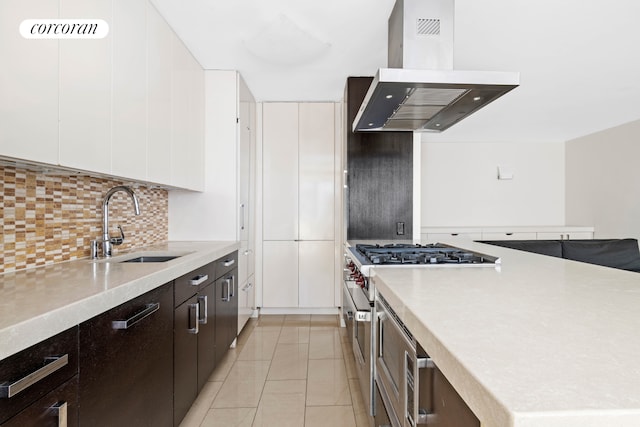 kitchen featuring decorative backsplash, white cabinets, high end stove, a sink, and island exhaust hood