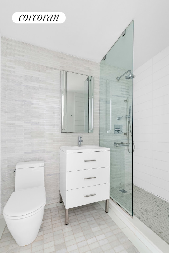 full bath featuring tile walls, tiled shower, toilet, and vanity