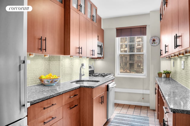 kitchen with a sink, appliances with stainless steel finishes, decorative backsplash, and dark stone countertops