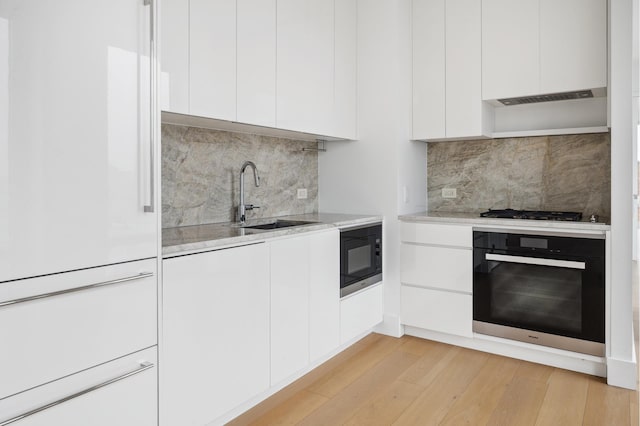 15 W 61st St Unit 27C, New York City, NY 10023 - kitchen with black appliances, modern cabinets, white cabinets, light wood-type flooring, and backsplash