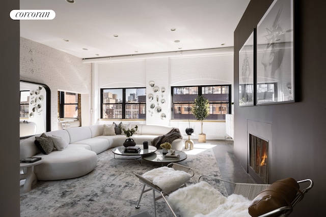 living area featuring concrete flooring, a warm lit fireplace, and brick wall